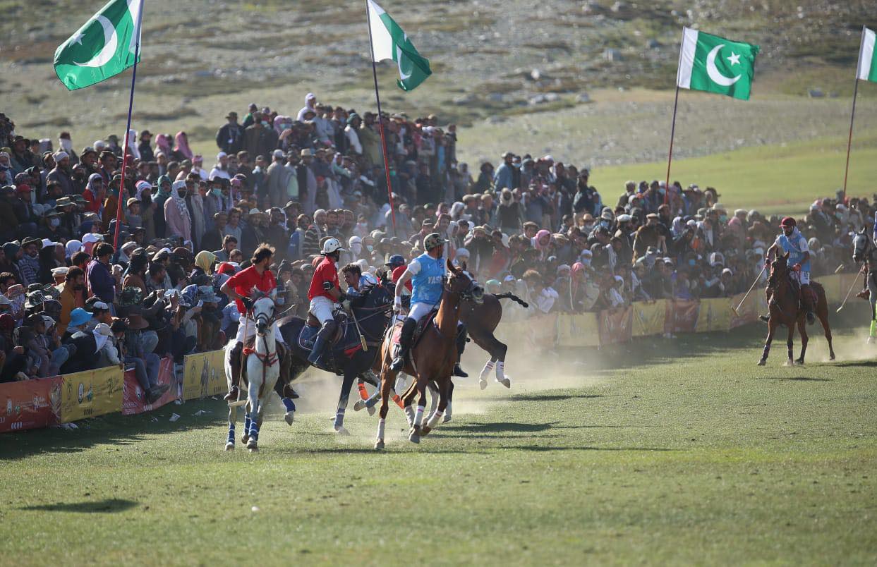 Polo riders contesting the ball beside spectators and Pakistan flags at Shandur