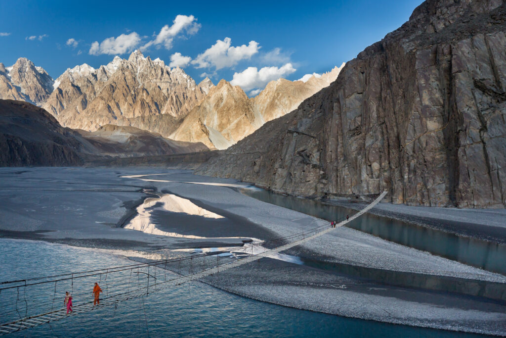 A broad mountain river winding beneath sunlit rock walls in northern Pakistan.