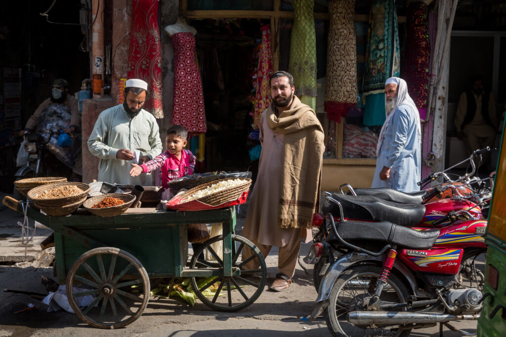 Street vendors and visitors gathered beside a small shop and cart in Pakistan.