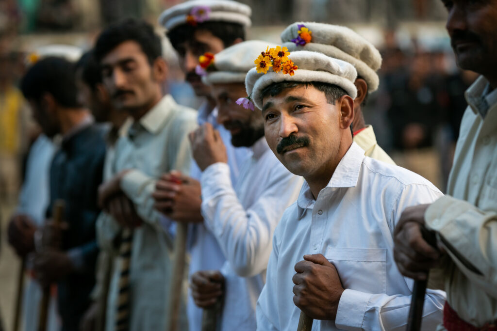 A man wearing a pakol decorated with flowers amid a gathering in northern Pakistan.