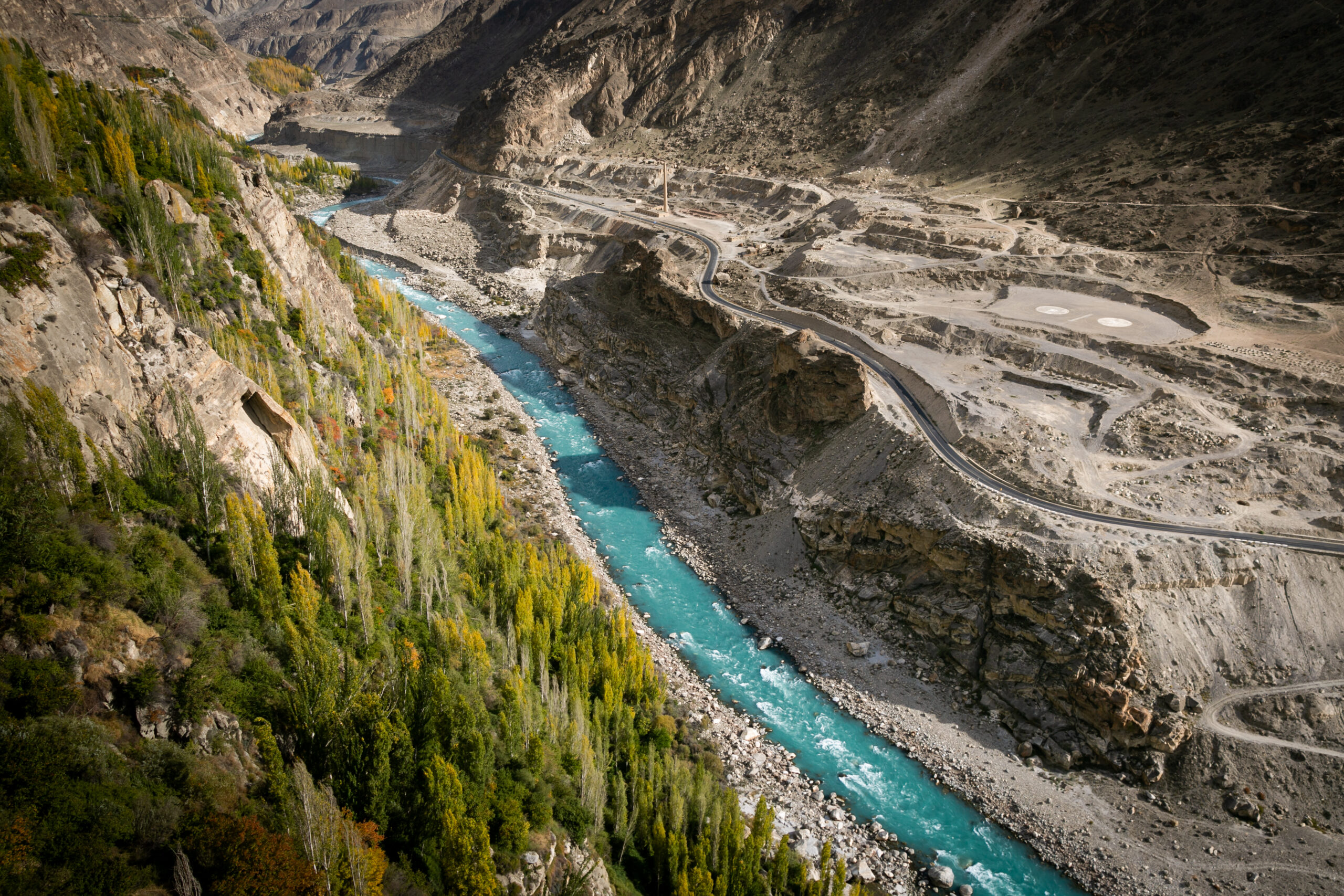 Autumn poplars lining a braided river beneath steep mountain slopes in northern Pakistan.