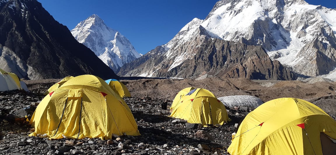 Yellow expedition tents pitched among rocks beneath snow-covered Karakoram peaks in Pakistan.