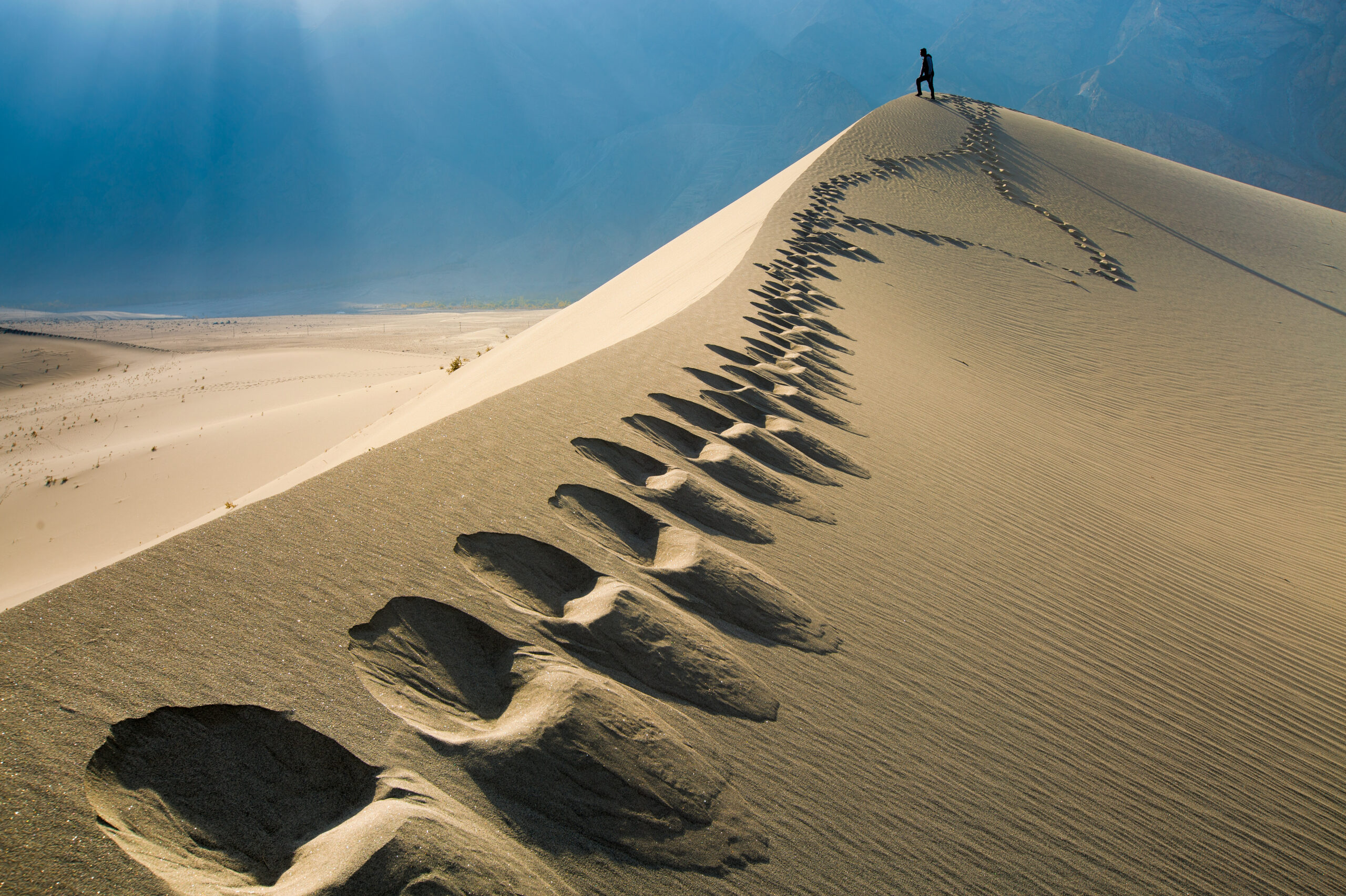 A walker on a sand dune beneath the mountain backdrop at Katpana, Skardu.