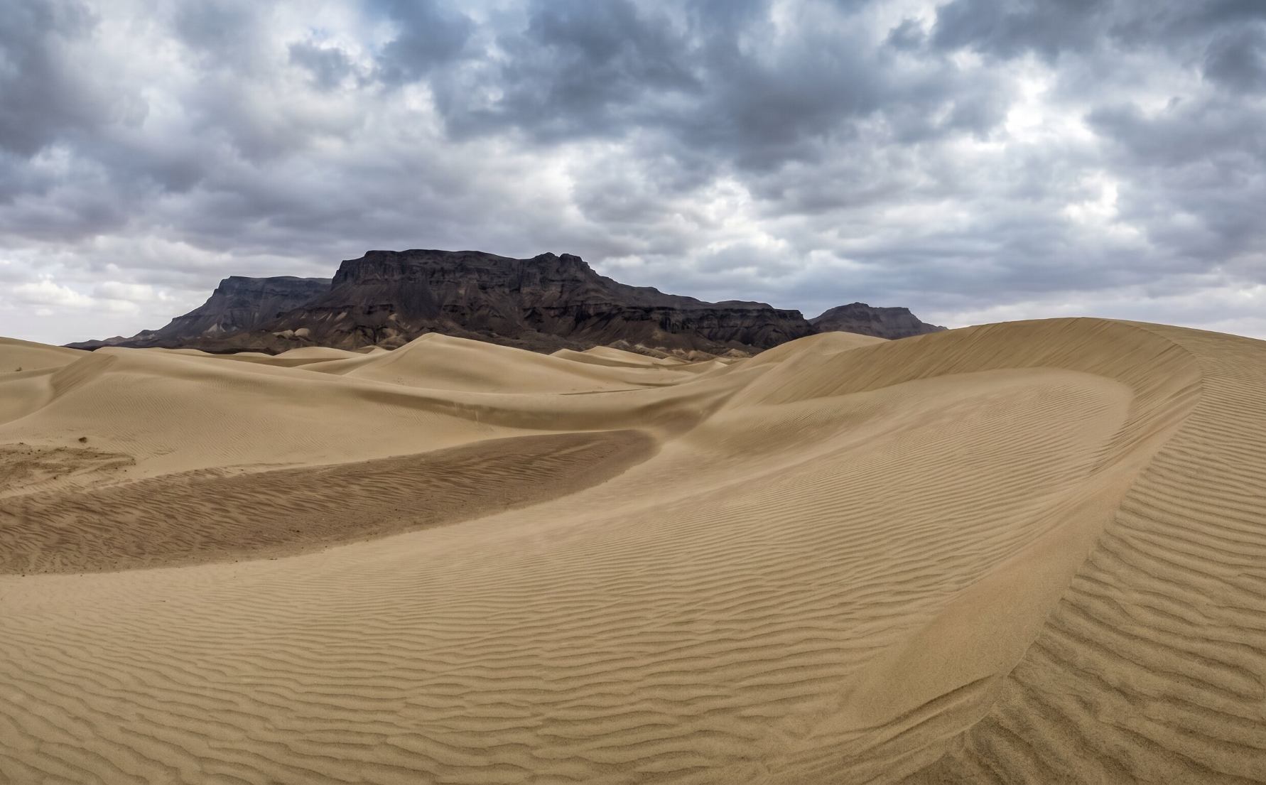 The stark and remote Kharan Desert in Balochistan Pakistan with large shifting sand dunes against a dramatic cloudy sky and mountain range in the background