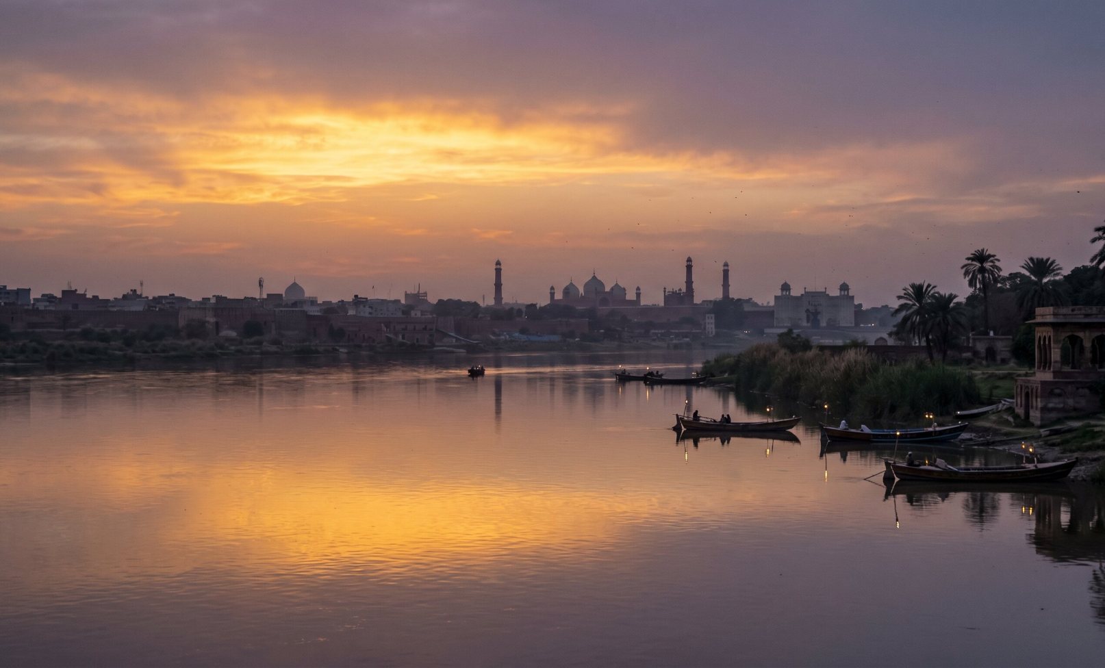 The Ravi River flowing past Lahore Pakistan at dusk with the silhouette of Mughal architecture on the distant bank and golden sky above