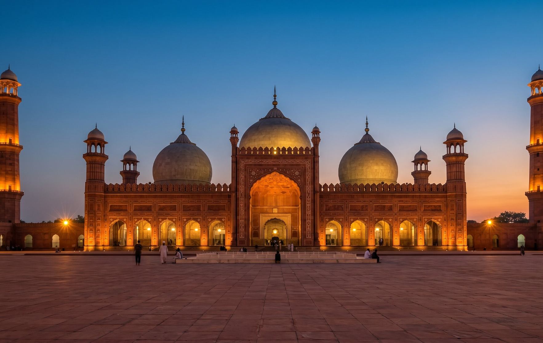 Badshahi Mosque in Lahore Pakistan at dusk with its four minarets lit against a deep blue and orange sunset sky