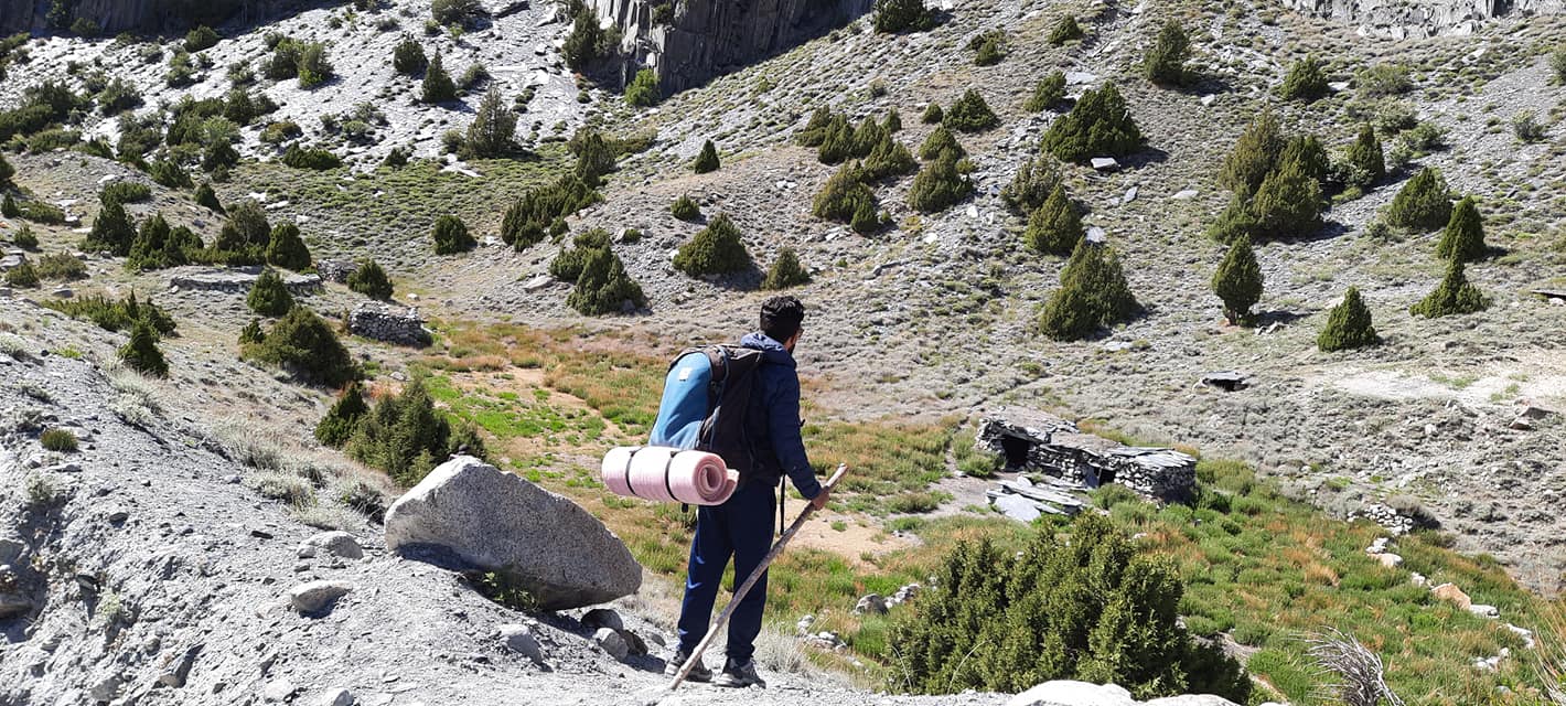 Trekker carrying a pack towards a stone shelter on the Patundas route